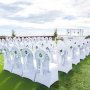 białe krzesła z pokrowcami z elastycznego spandexu VEVOR i srebrnymi szarfami przygotowane na wesele na świeżym powietrzu.