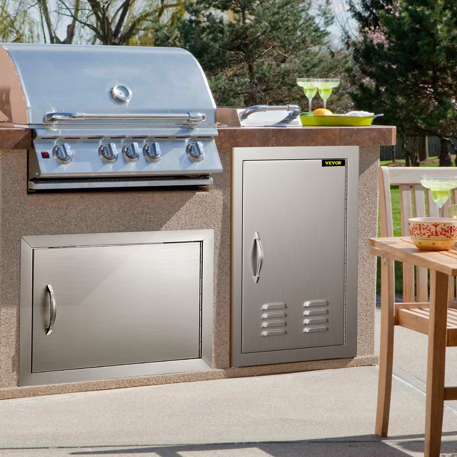 stainless steel VEVOR outdoor kitchen doors next to grill, with trees in the background.