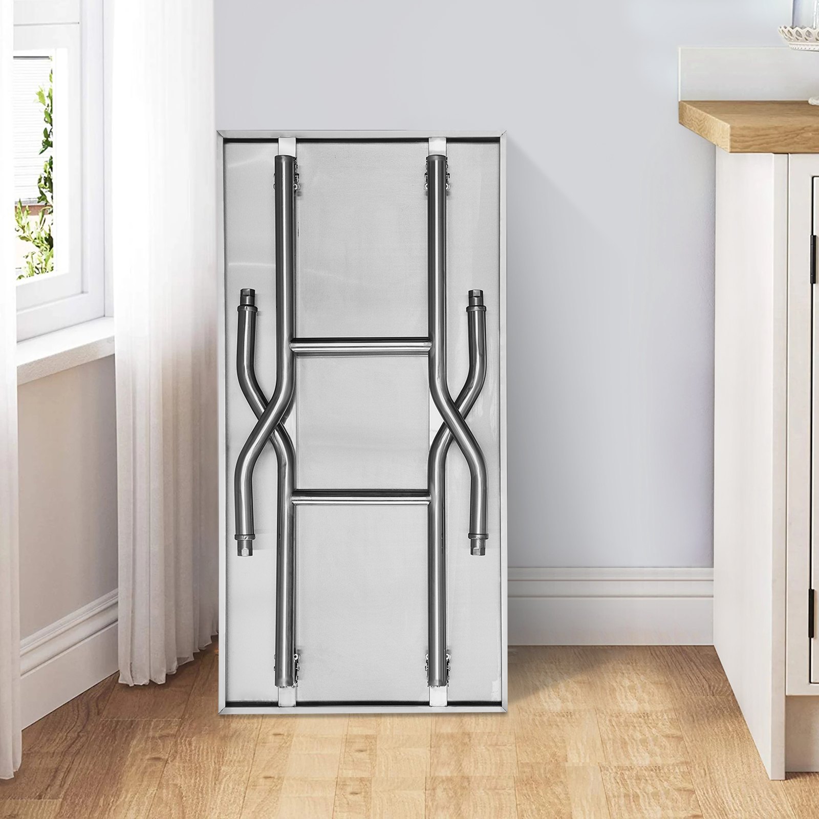 folded VEVOR commercial worktable leaning against a kitchen wall, next to the window.