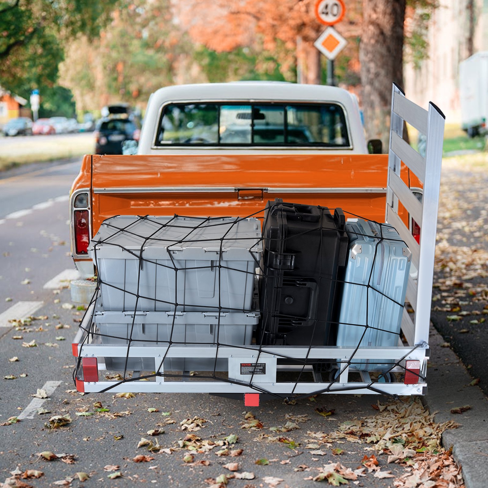 orange and white truck with a VEVOR hitch cargo carrier loaded with boxes and luggage on a leafy street.