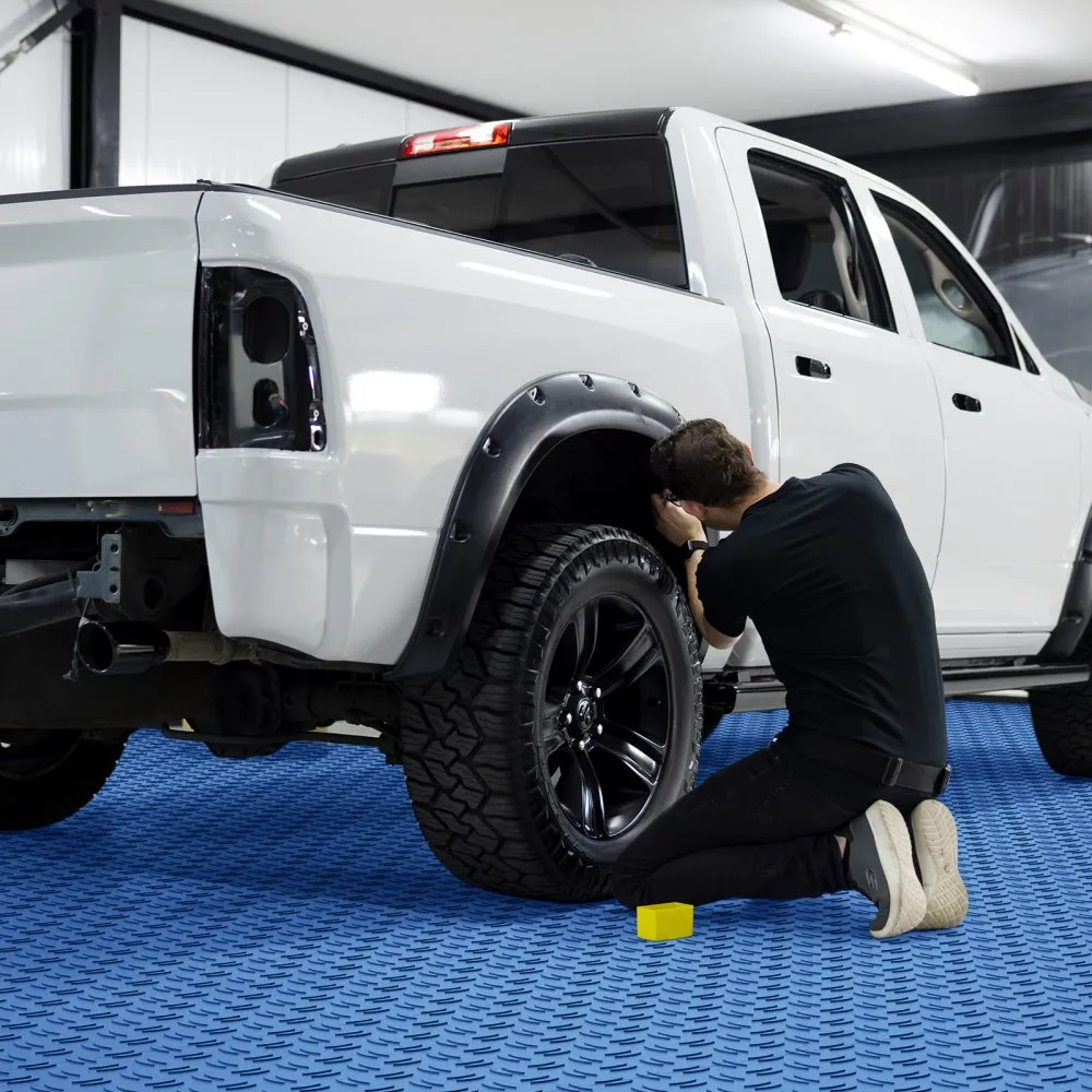 mechanic working on a white pickup truck with VEVOR garage tiles in a brightly lit garage.