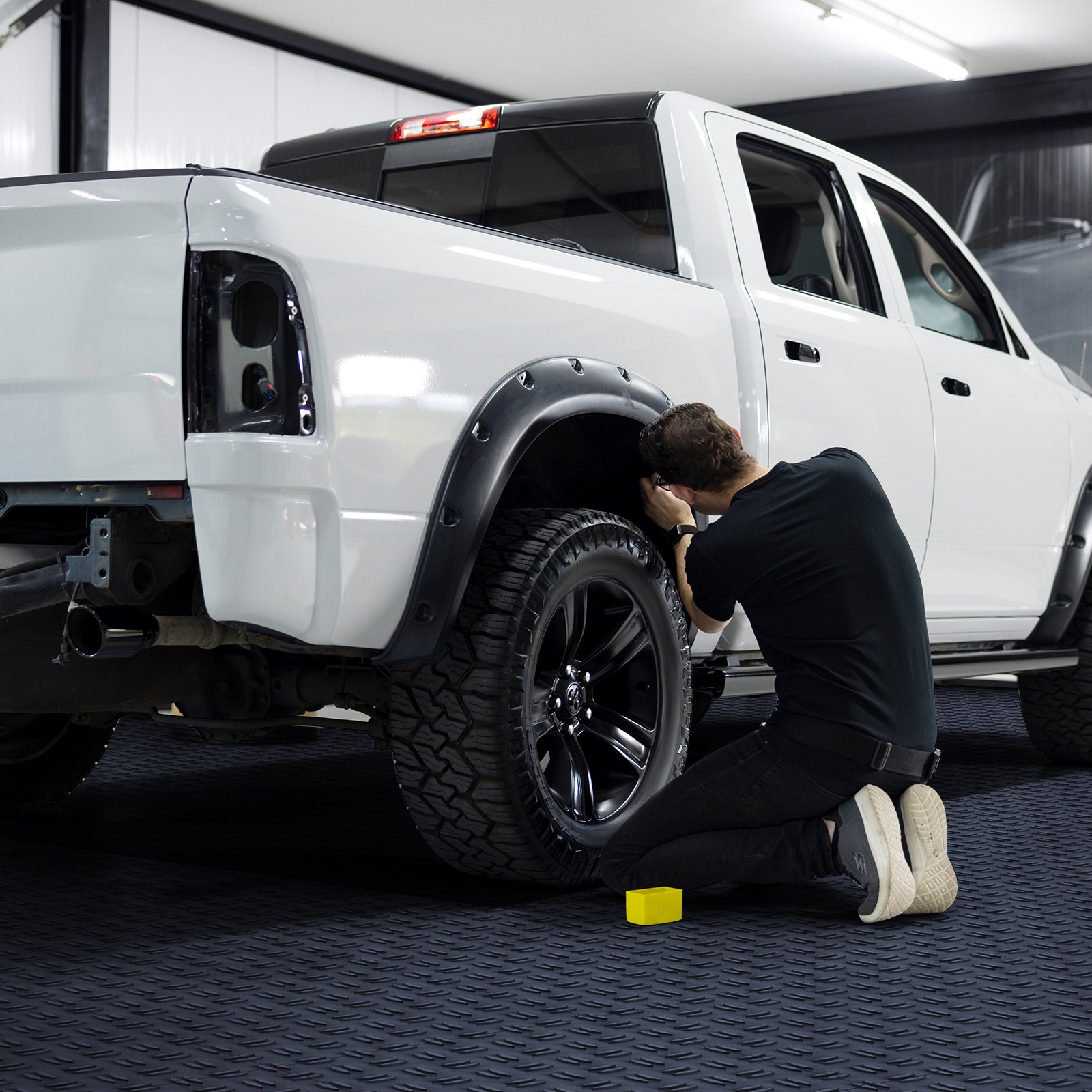 mechanic working on a white truck in a garage with VEVOR garage tiles.