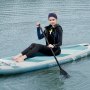 person sitting on a VEVOR inflatable paddle board in the water, holding a paddle, wearing a wetsuit.