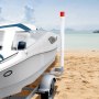 boat on a trailer with a VEVOR marine trailer guide set at a sandy beach, calm sea, and cloudy sky.