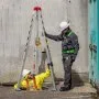 two workers using VEVOR confined space tripod kit, one in yellow suit entering a manhole and man in gray suit.