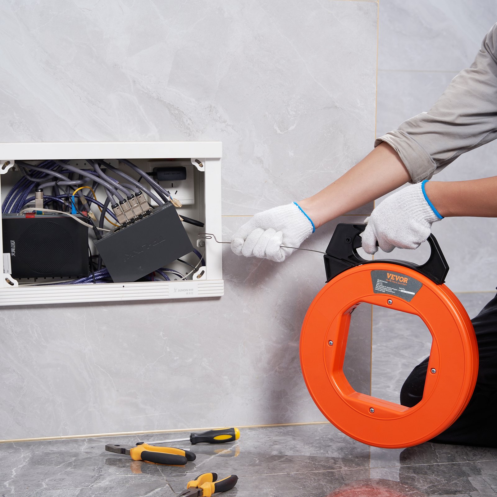 person using VEVOR fish tape to manage electrical wiring inside a wall panel.