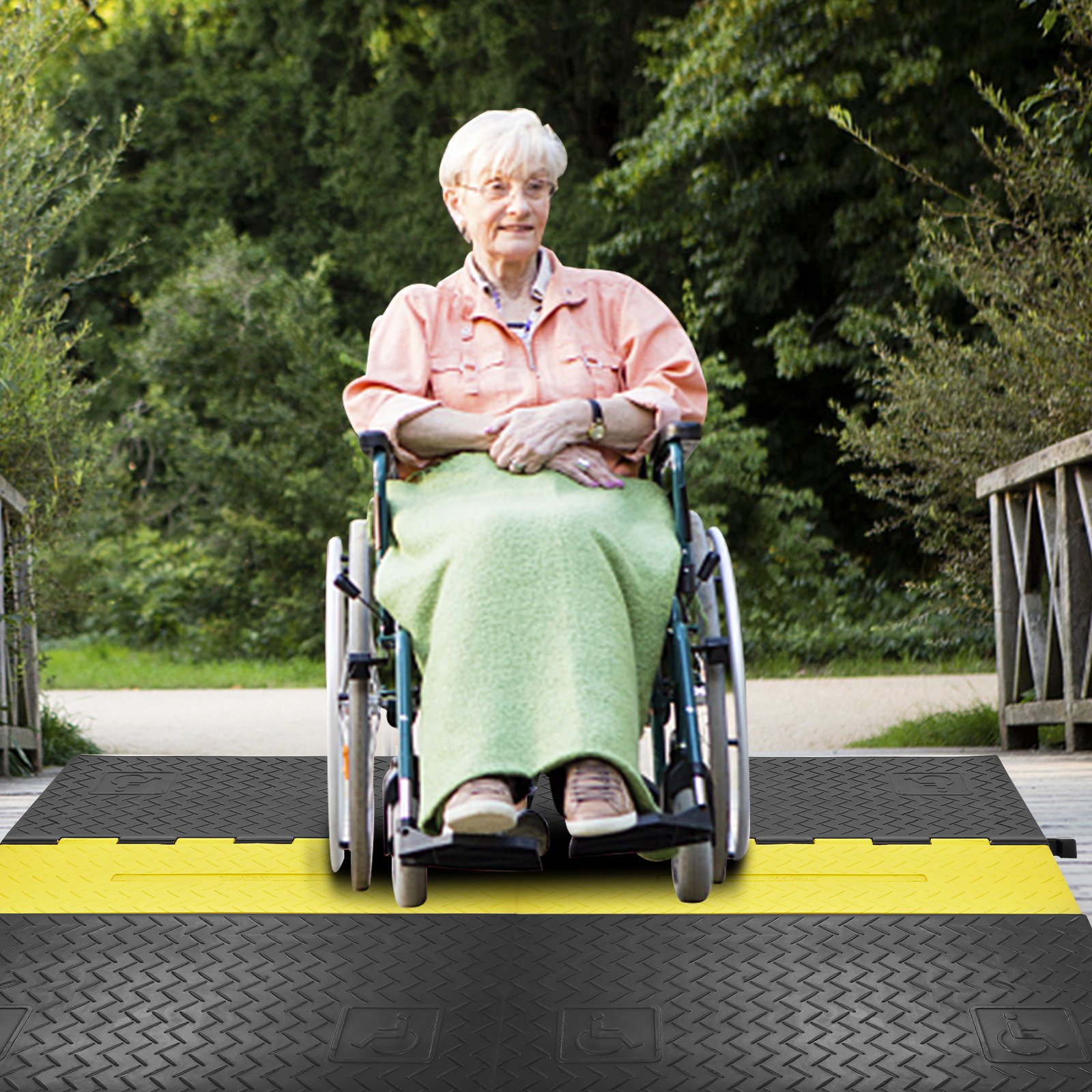 person in wheelchair using VEVOR cable protector ramp on outdoor pathway, surrounded by greenery.