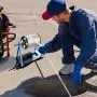 man using VEVOR polyester pull tape for underground work near a manhole with protective gloves.