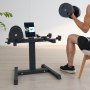 man exercising with dumbbells next to a VEVOR dumbbell stand holding a tablet in a bright room.