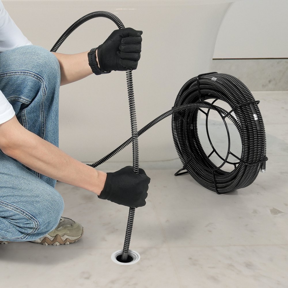 man using VEVOR drain cleaning cable to unclog a drain, wearing black gloves and jeans, with cable reel.