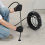man using VEVOR drain cleaning cable to unclog a drain, wearing black gloves and jeans, with cable reel.