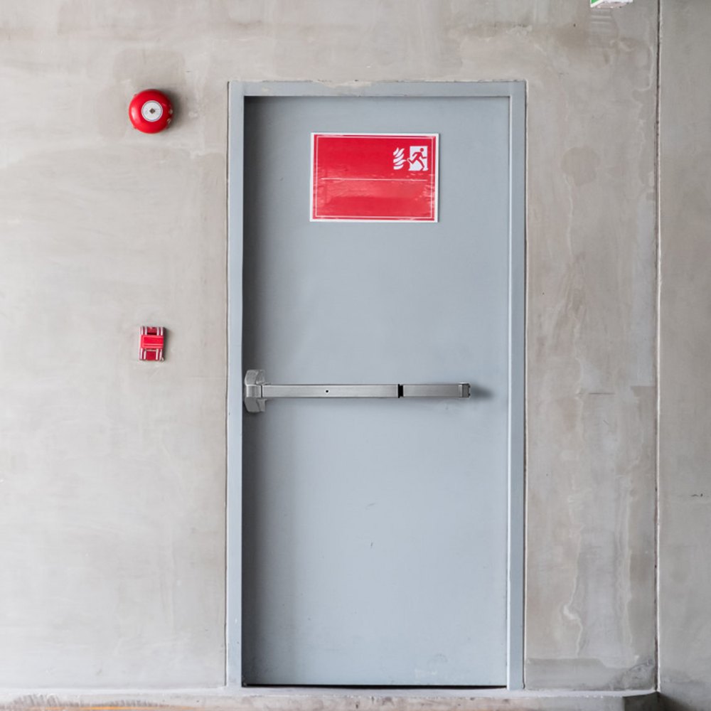 gray door with a VEVOR panic exit device, red exit sign above, and fire alarm equipment nearby.