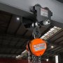 VEVOR manual trolley attached to an overhead beam in an industrial warehouse.