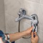 person using VEVOR pipe wrench to tighten a bathroom faucet against tiled wall.