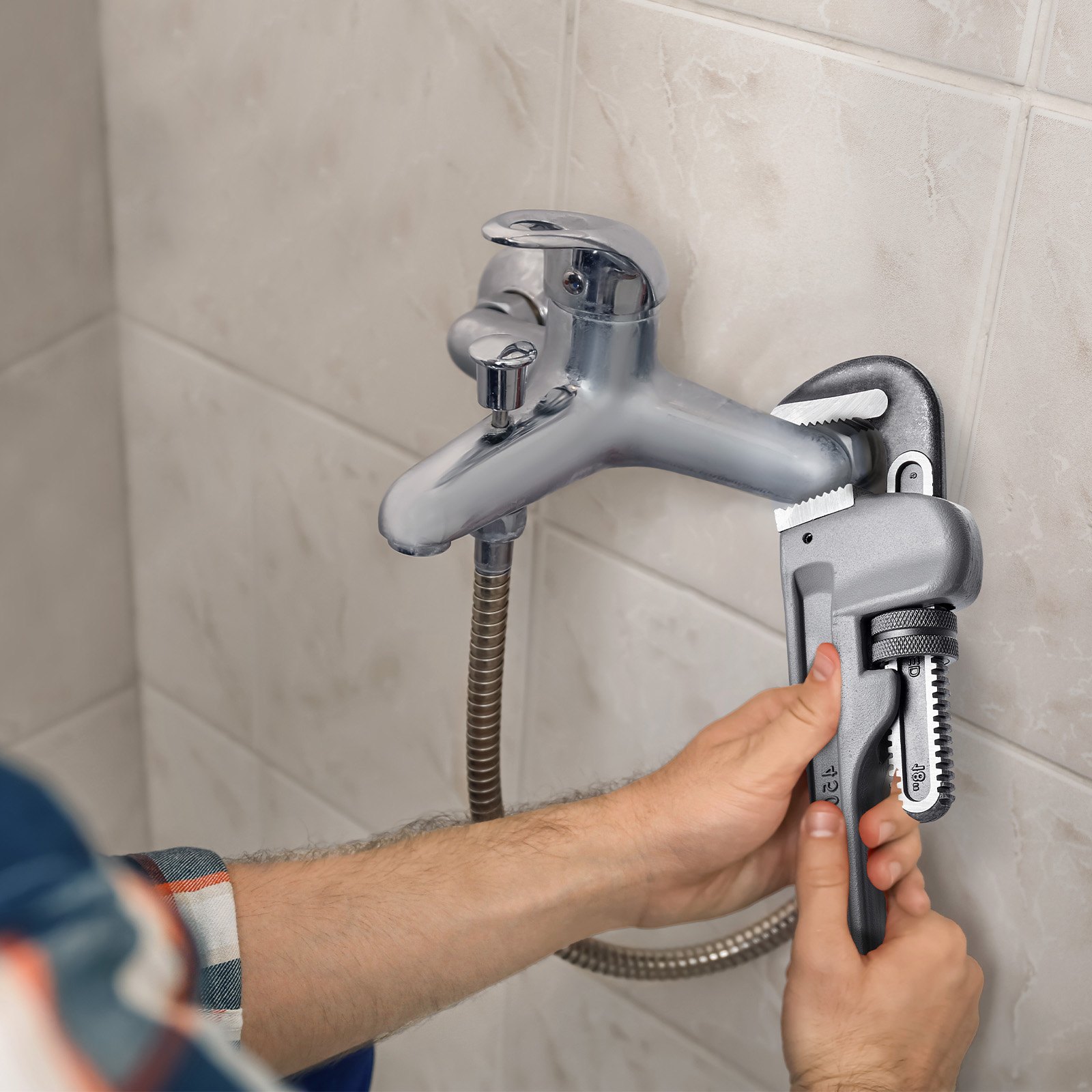 person using VEVOR pipe wrench to tighten a bathroom faucet against tiled wall.