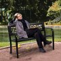 person relaxing on a VEVOR outdoor bench by a pond, surrounded by lush greenery in a serene park setting.