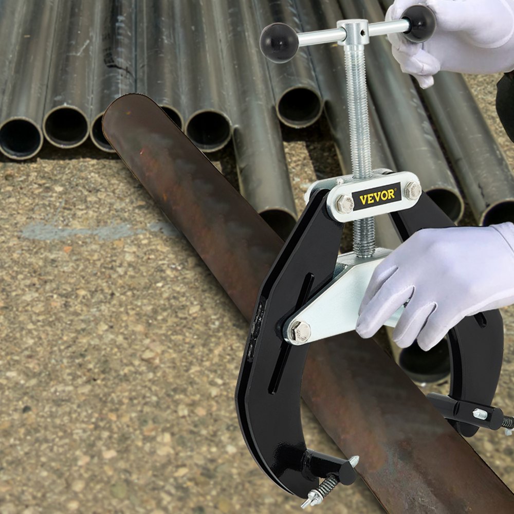 VEVOR pipe clamp securing large pipe with gloved hands, background of stacked metal pipes on concrete.