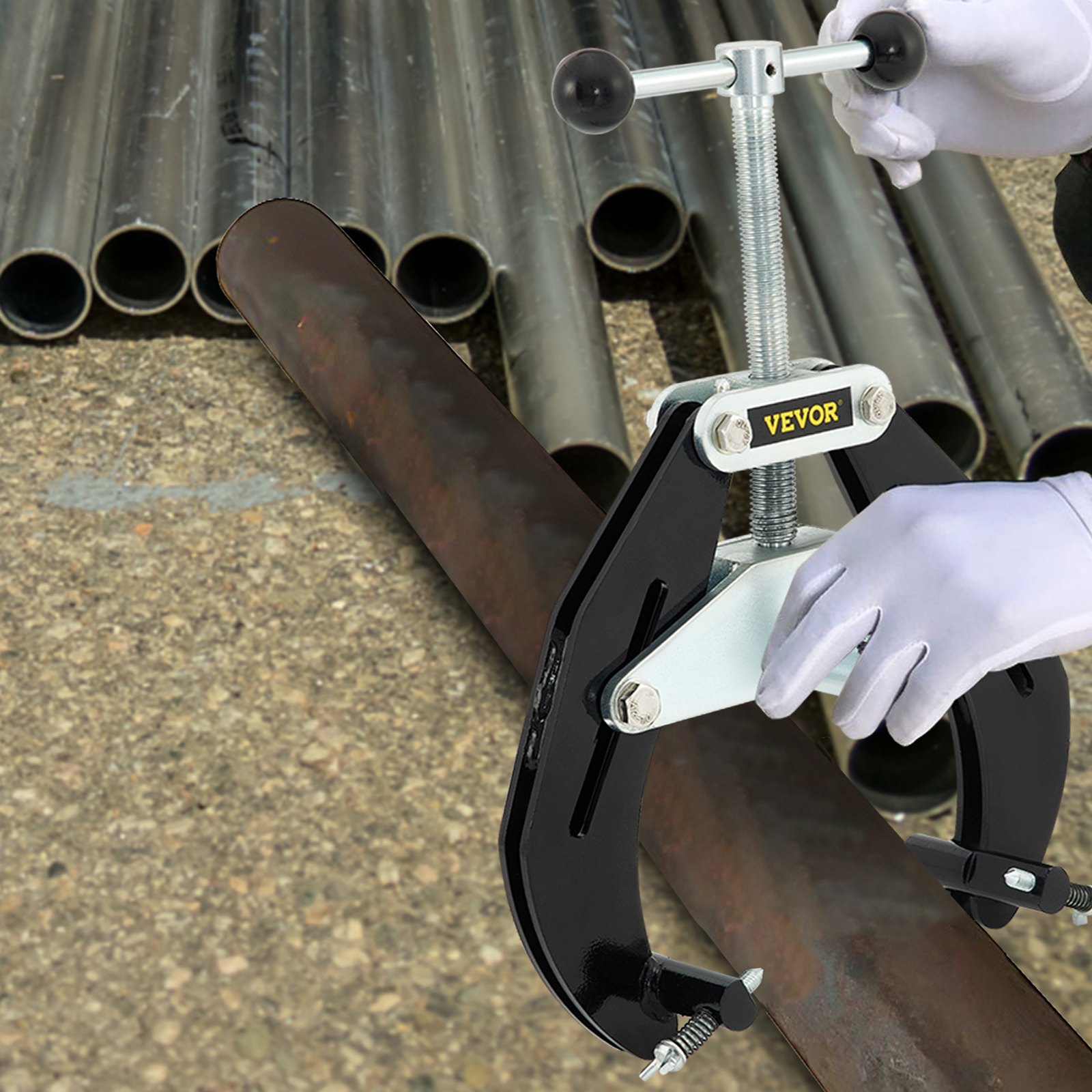 VEVOR pipe clamp securing large pipe with gloved hands, background of stacked metal pipes on concrete.