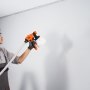 Persona que utiliza un pulverizador de pintura VEVOR, con guantes, pintando una pared blanca.