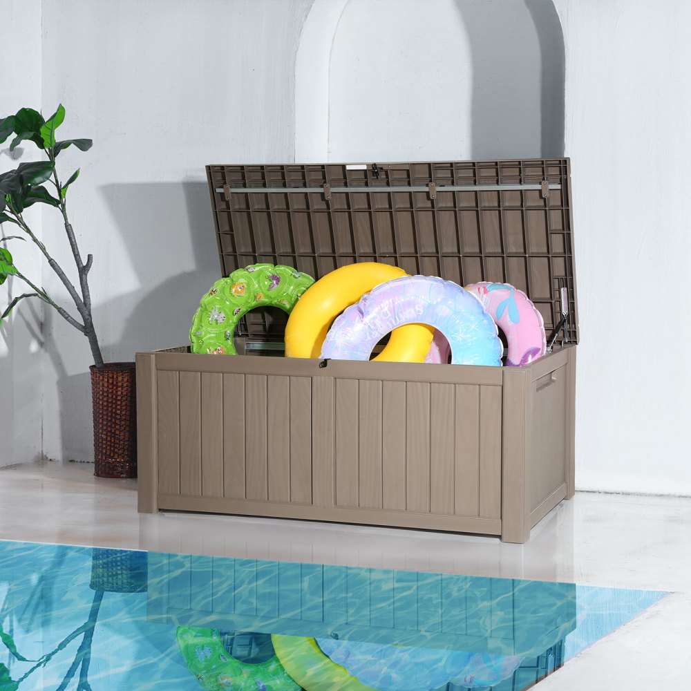 VEVOR deck box by a pool, open lid, storing colorful floaties, plant in the background.