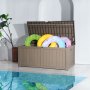 VEVOR deck box by a pool, open lid, storing colorful floaties, plant in the background.