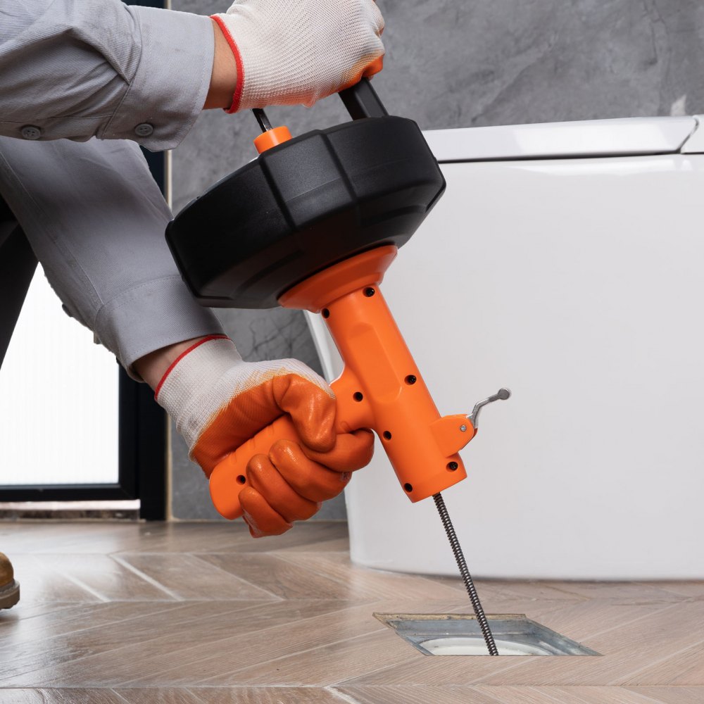 person using VEVOR drain auger to unclog a floor drain near a toilet.
