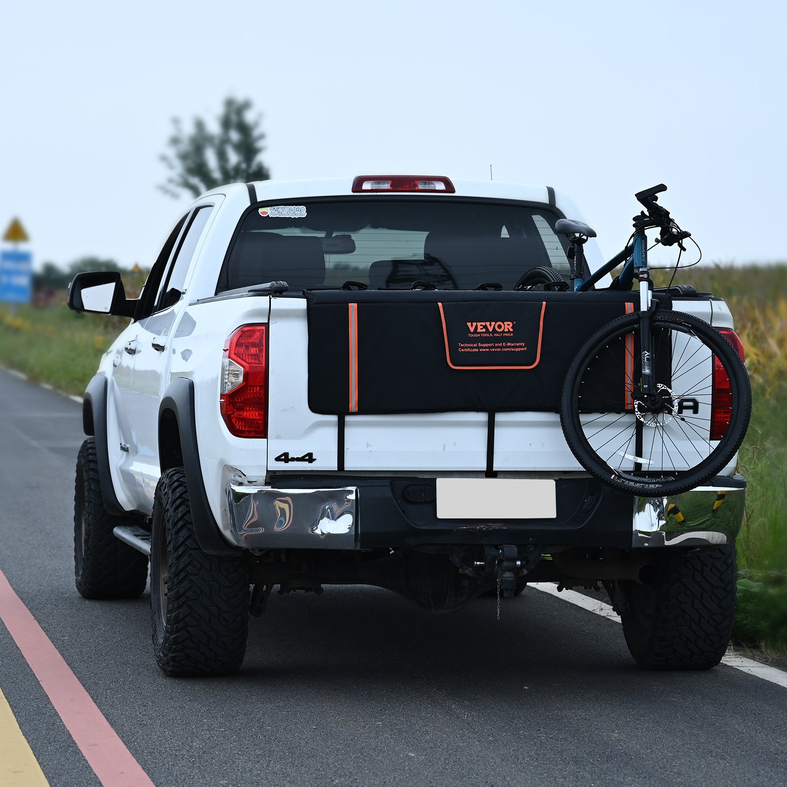 white pickup truck with a VEVOR tailgate pad securing a black bicycle on a rural road.