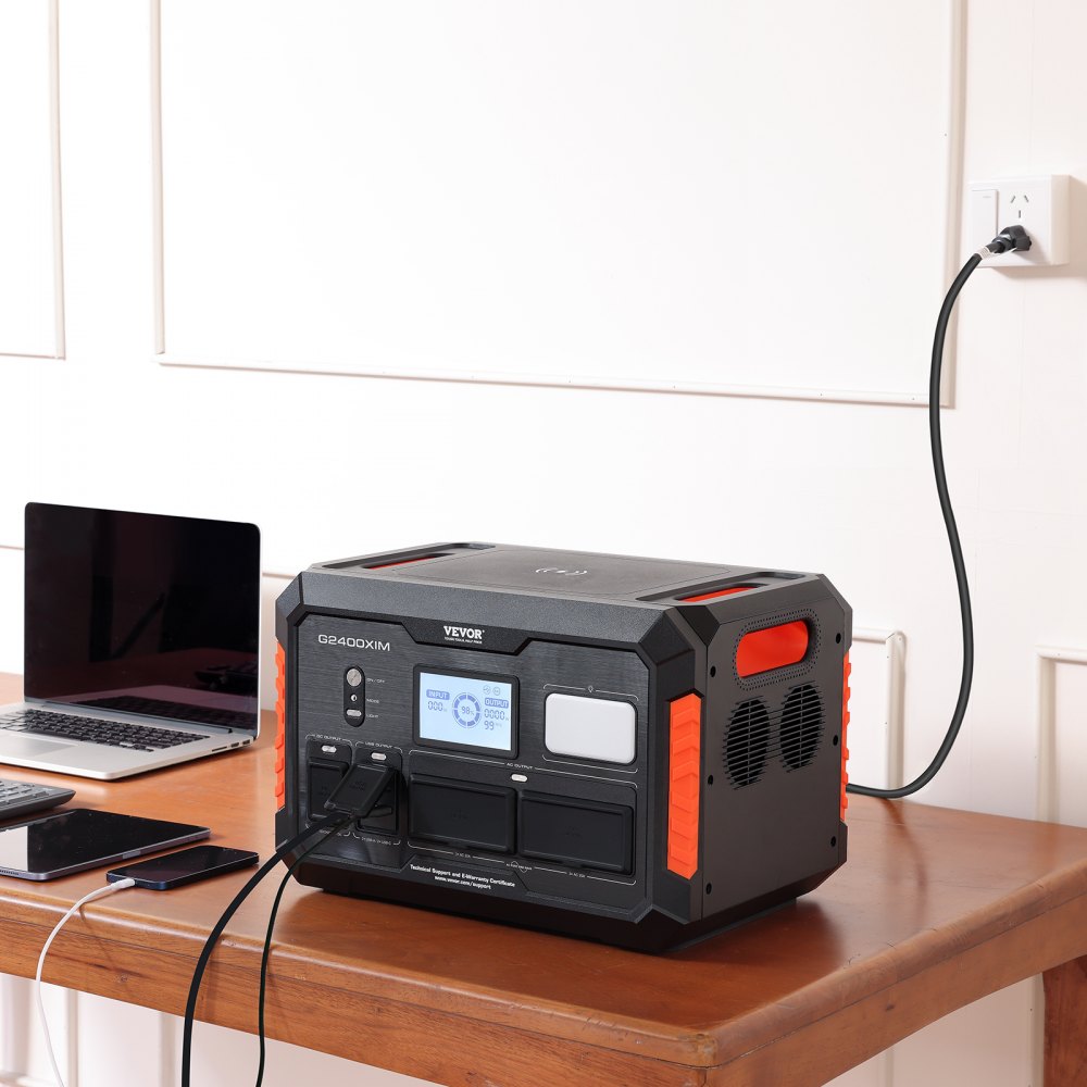 Estación de energía portátil VEVOR que carga dispositivos sobre un escritorio de madera con una computadora portátil y teléfonos inteligentes al lado.