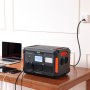 Estación de energía portátil VEVOR que carga dispositivos sobre un escritorio de madera con una computadora portátil y teléfonos inteligentes al lado.