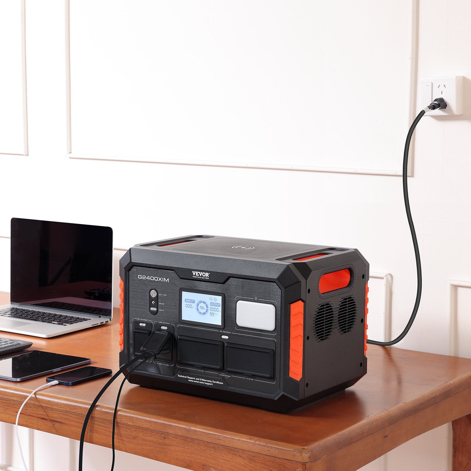 Estación de energía portátil VEVOR que carga dispositivos sobre un escritorio de madera con una computadora portátil y teléfonos inteligentes al lado.
