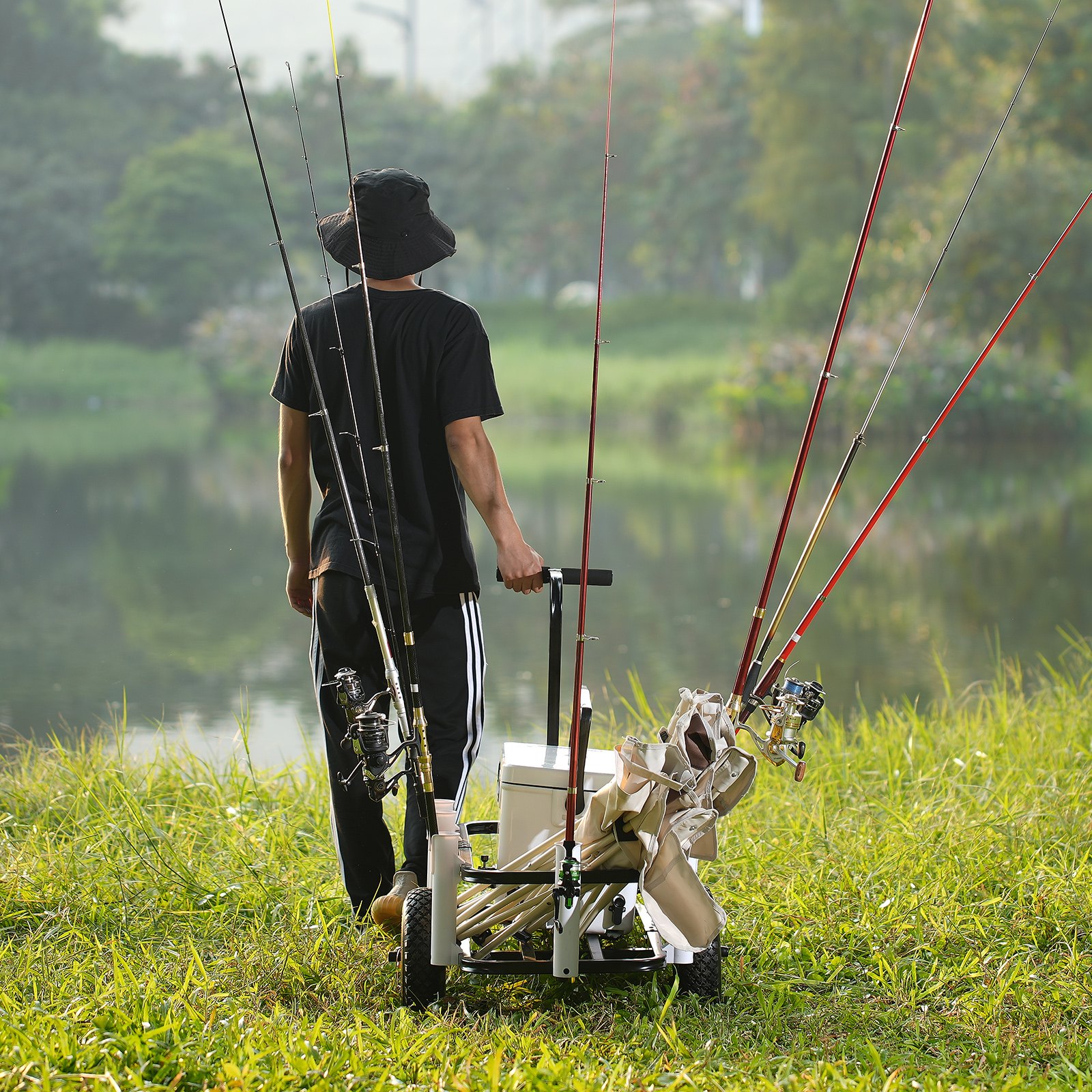 man pulling a VEVOR beach fishing cart loaded with fishing rods near a lakeside.