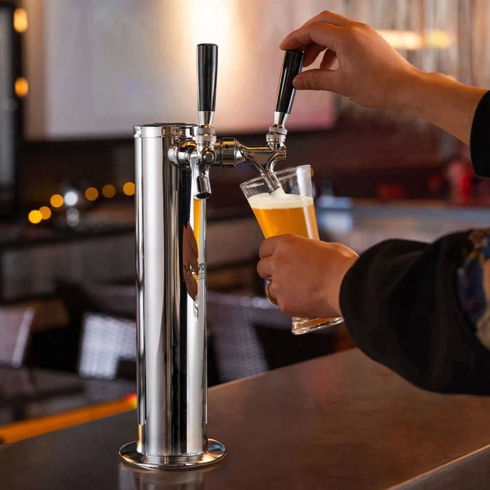 hand pouring beer from VEVOR dual taps draft beer tower on a countertop in a dimly lit bar.