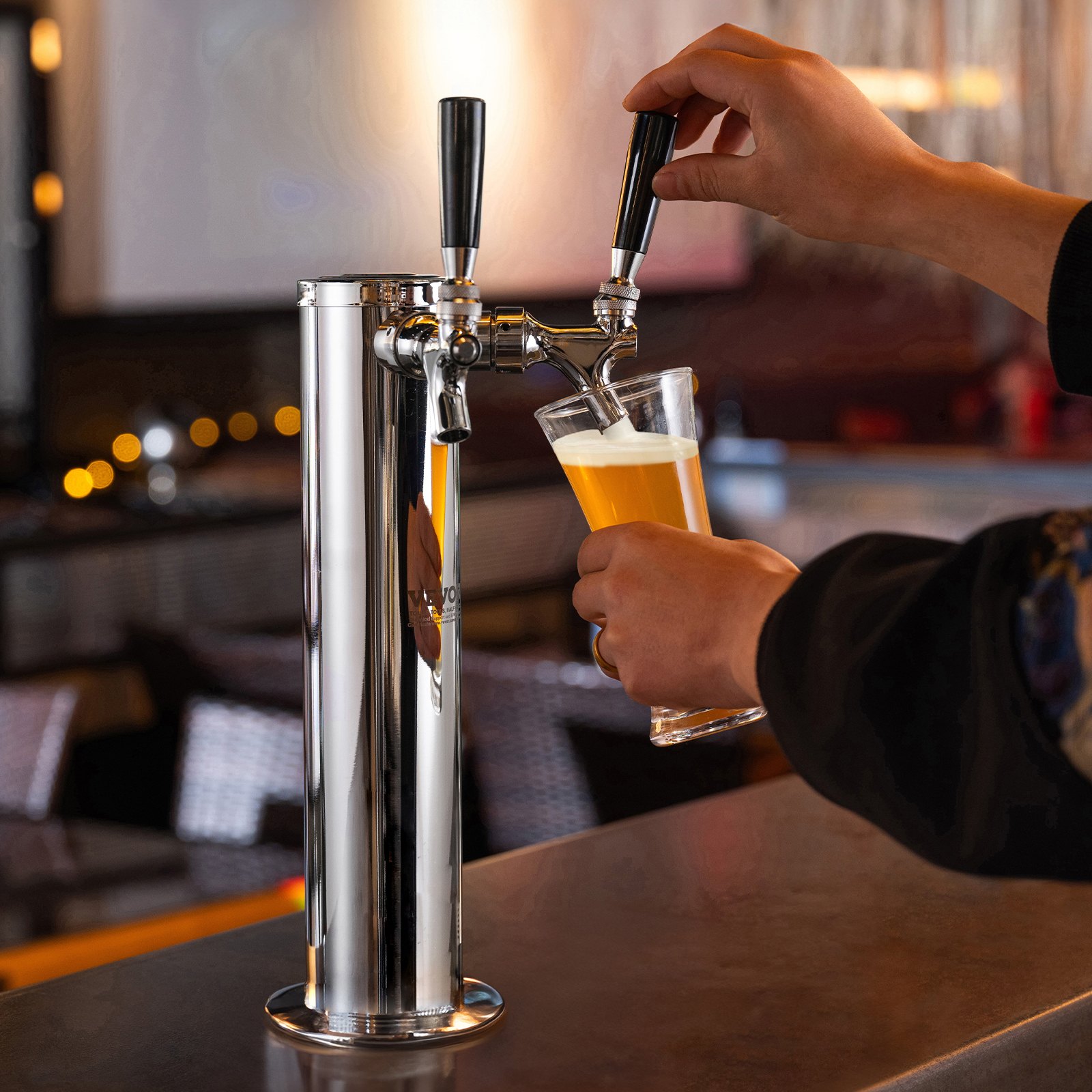 hand pouring beer from VEVOR dual taps draft beer tower on a countertop in a dimly lit bar.