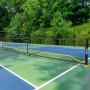 VEVOR pickleball net set up on a multi-color outdoor court surrounded by lush green trees.