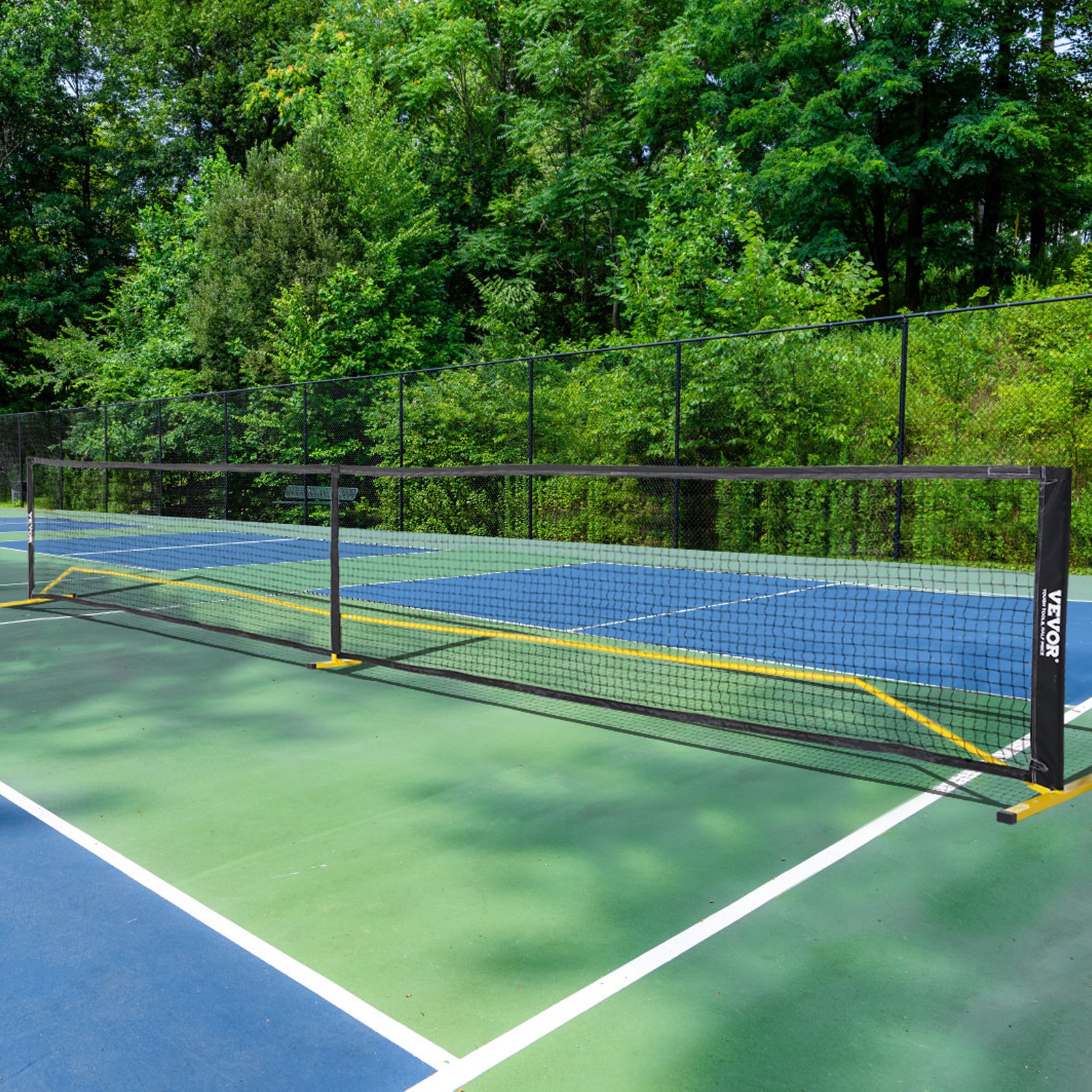 VEVOR pickleball net set up on a multi-color outdoor court surrounded by lush green trees.
