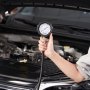hand holding VEVOR diesel engine compression tester in front of an open car hood.