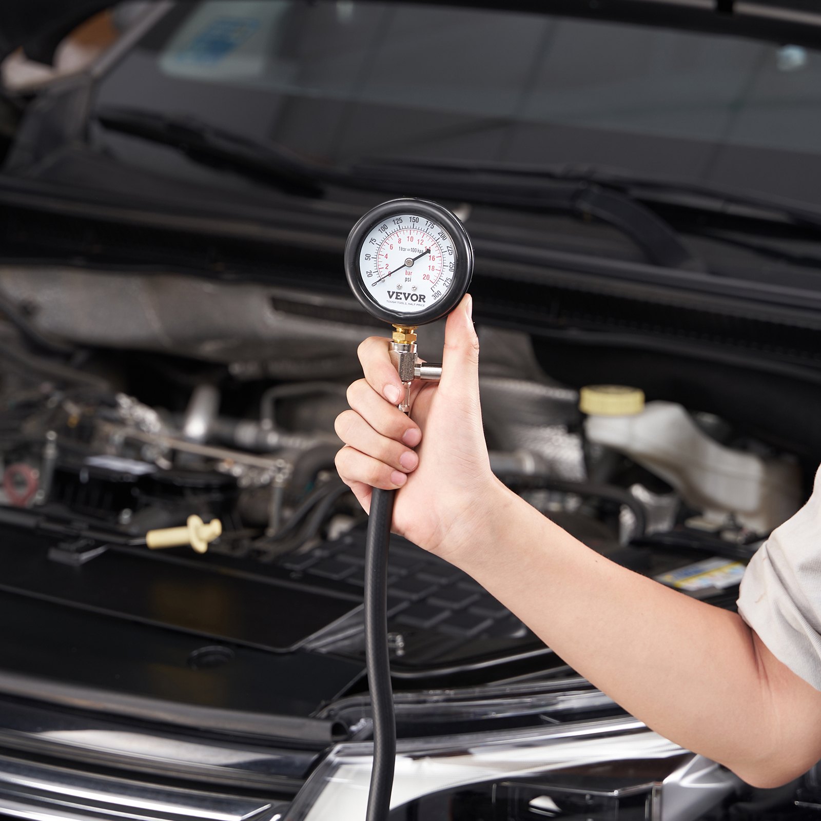 hand holding VEVOR compression tester kit gauge in front of open car hood.