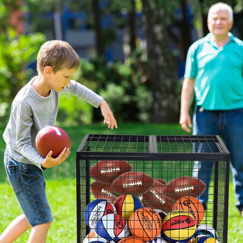 child playing with football near VEVOR sports ball storage cart filled with various sports balls outside.