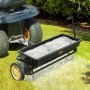 VEVOR seed spreader attached to a lawn tractor distributing seeds evenly over a green lawn.