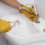 person using VEVOR groove joint pliers to fix a sink faucet, wearing yellow gloves.