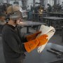 welder holding a VEVOR welding blanket in an industrial workshop setting with colleagues welding in the background.