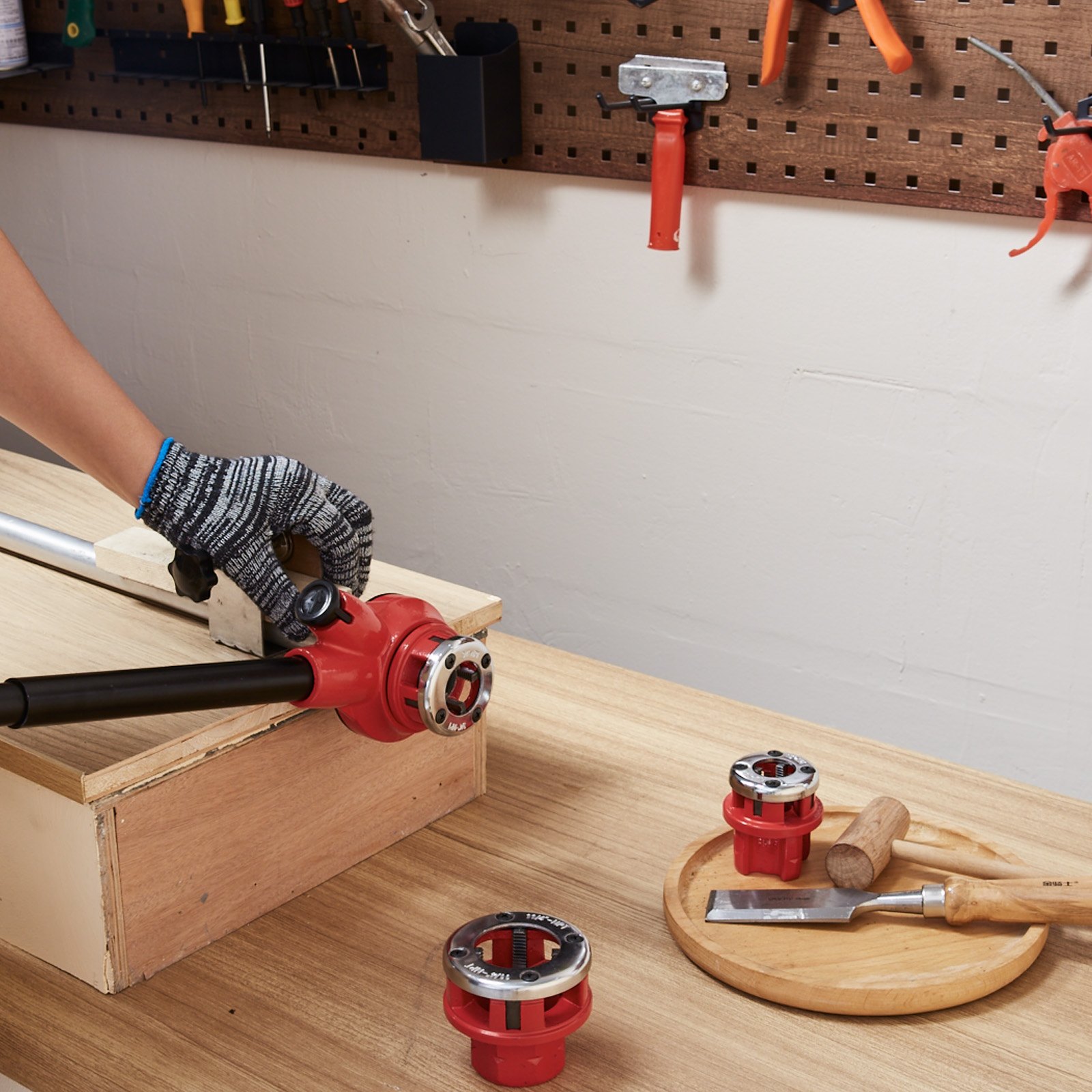 person using the red VEVOR pipe threader kit on a wooden bench with tools and pipe dies.