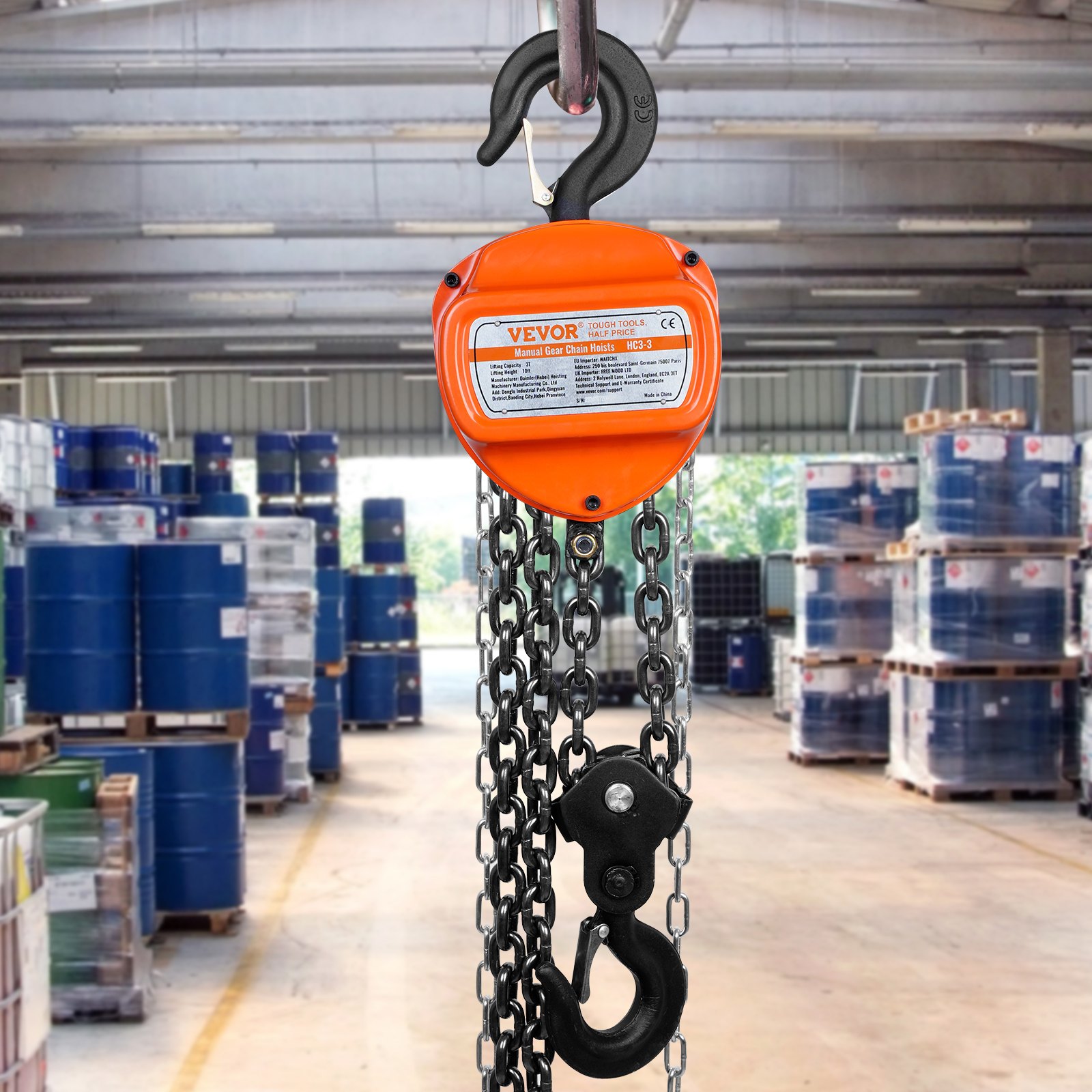 VEVOR hand chain hoist in a warehouse with stacked industrial barrels and pallets.