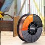 VEVOR mig welding wire spool next to a worker welding metal with sparks flying.