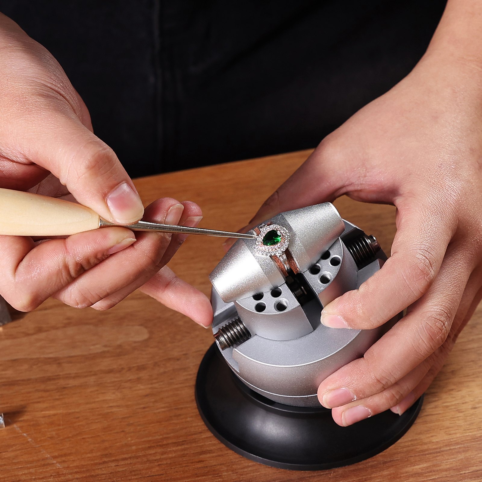 crafting jewelry using the VEVOR ball vise on a wooden table, focusing on a ring with a green gemstone.