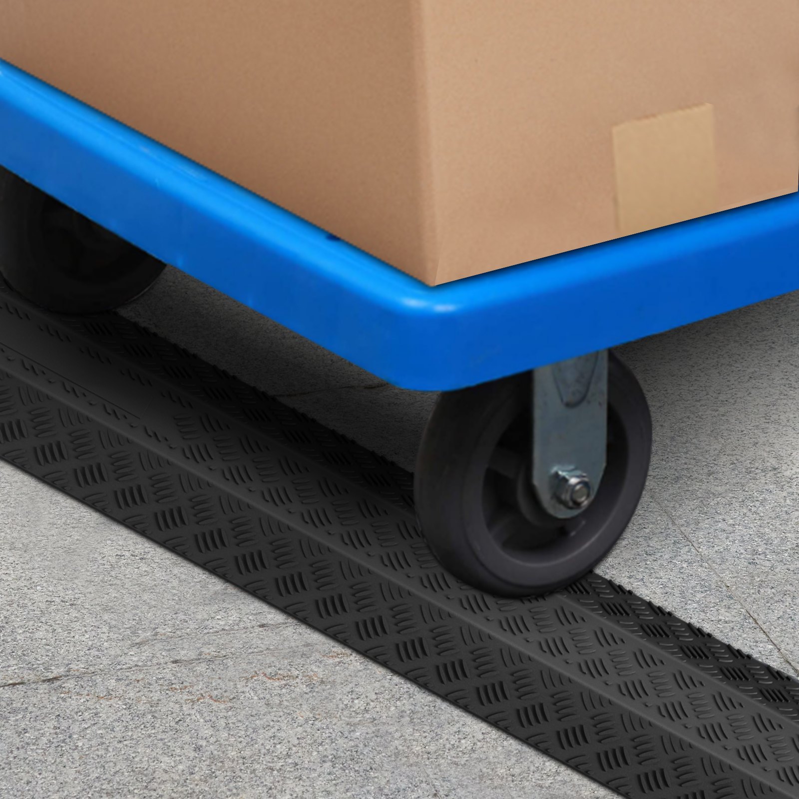 blue cart wheel crossing a VEVOR speed bump on a concrete surface, carrying a cardboard box.