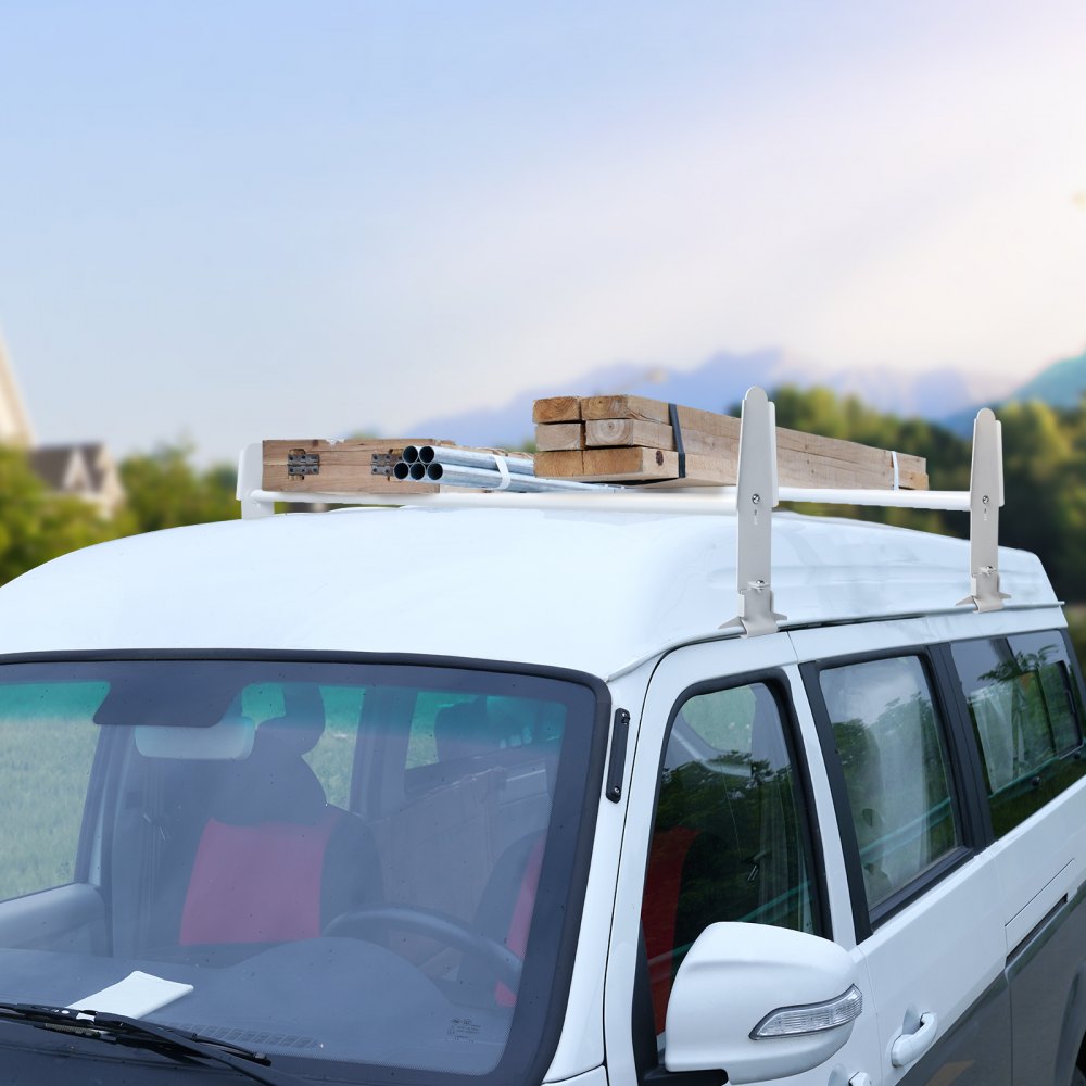 white van equipped with a VEVOR van roof ladder rack carrying lumber and pipes, with greenery in the background.