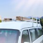 white van with VEVOR van ladder rack carrying wooden planks on the roof against a blurred background.