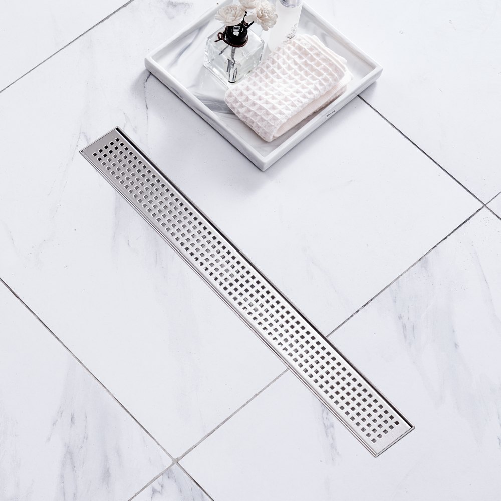 VEVOR linear shower drain on white marble tile floor with a tray, soap, and flowers nearby.