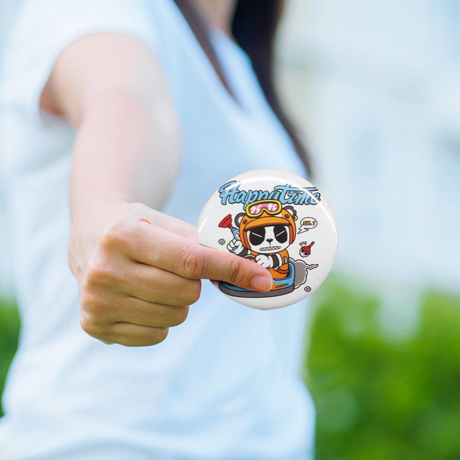 person holding a colorful pin-back button featuring a cartoon bear with &quot;happy time&quot; text.